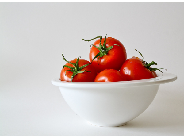 A white bowl of red tomatoes against a white background